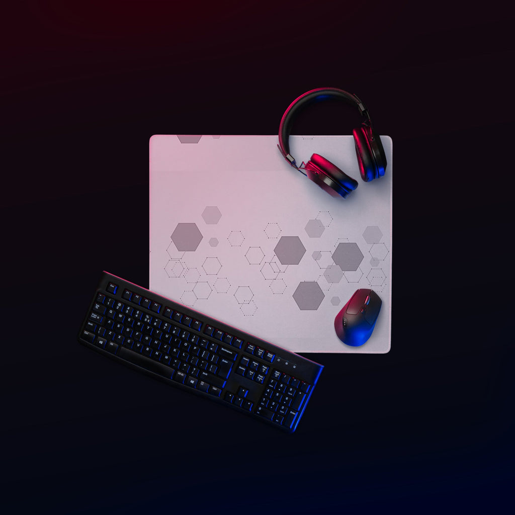 Key board, mouse and headphone on a grey gamer mouse pad with hexagonal pattern.