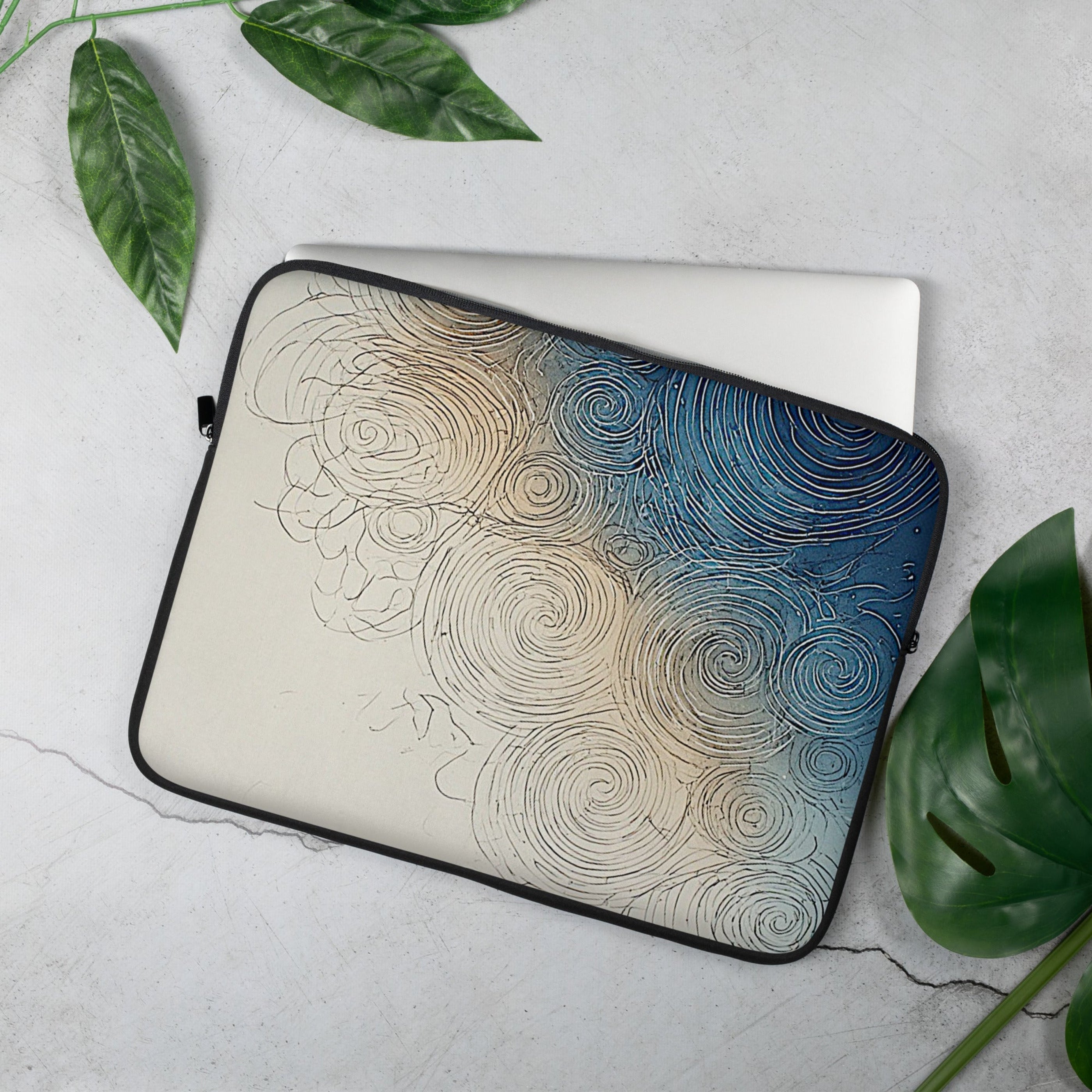 A laptop sleeve with an abstract spiral pattern in blue, beige, and black, shown on a light gray textured surface with green leaves around it.
