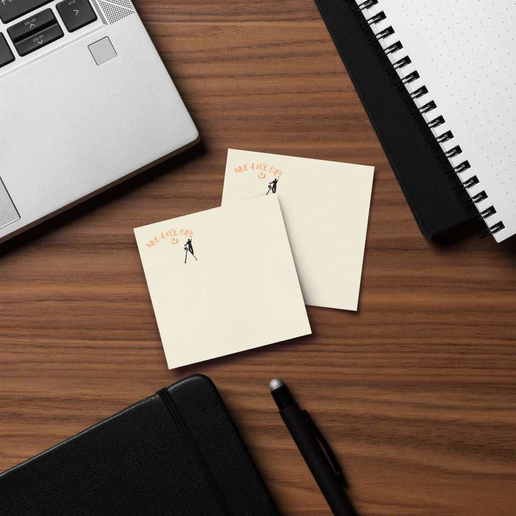 Two small notepads with illustrations on a wooden desk with a laptop and pen.
