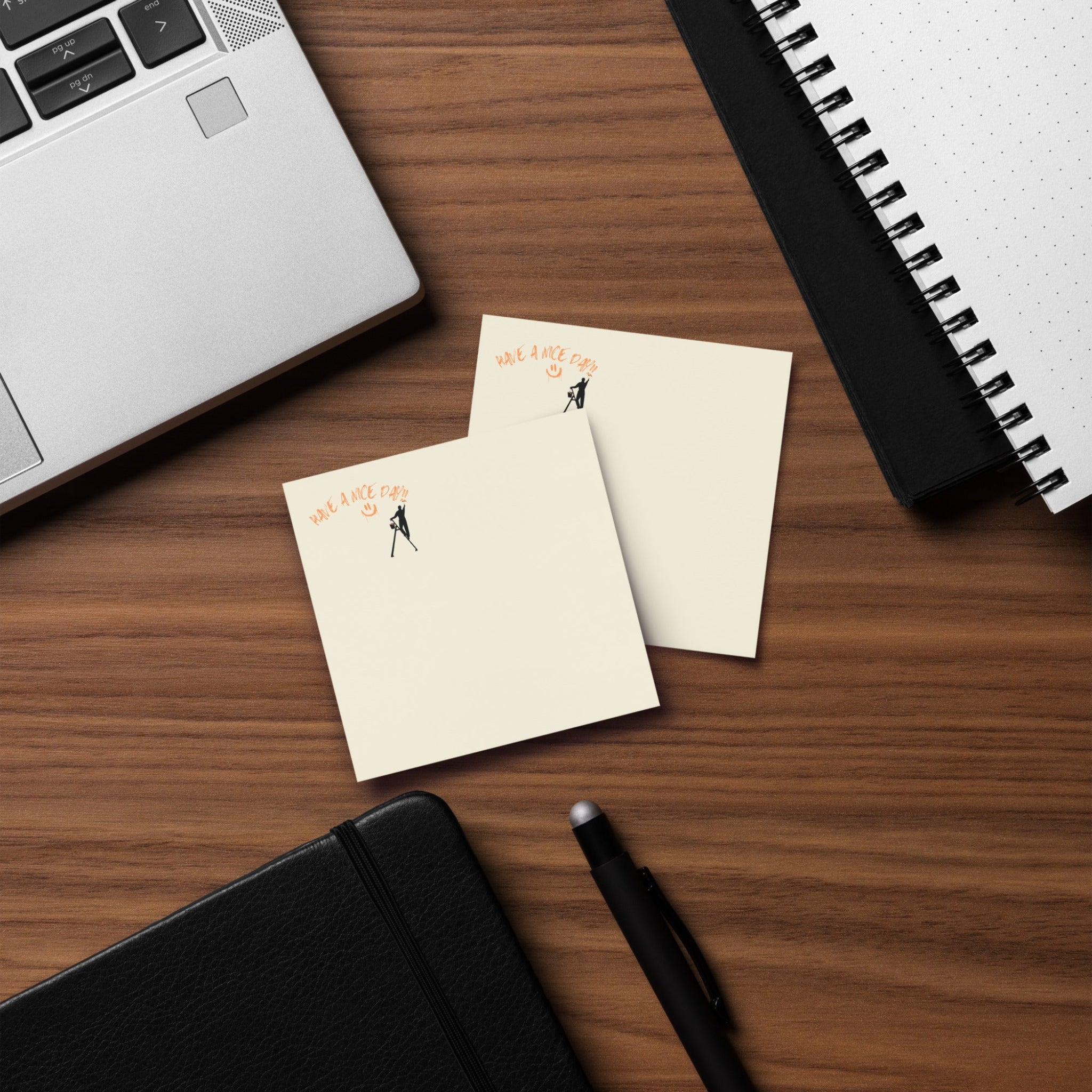 Two small notepads with illustrations on a wooden desk with a laptop and pen.
