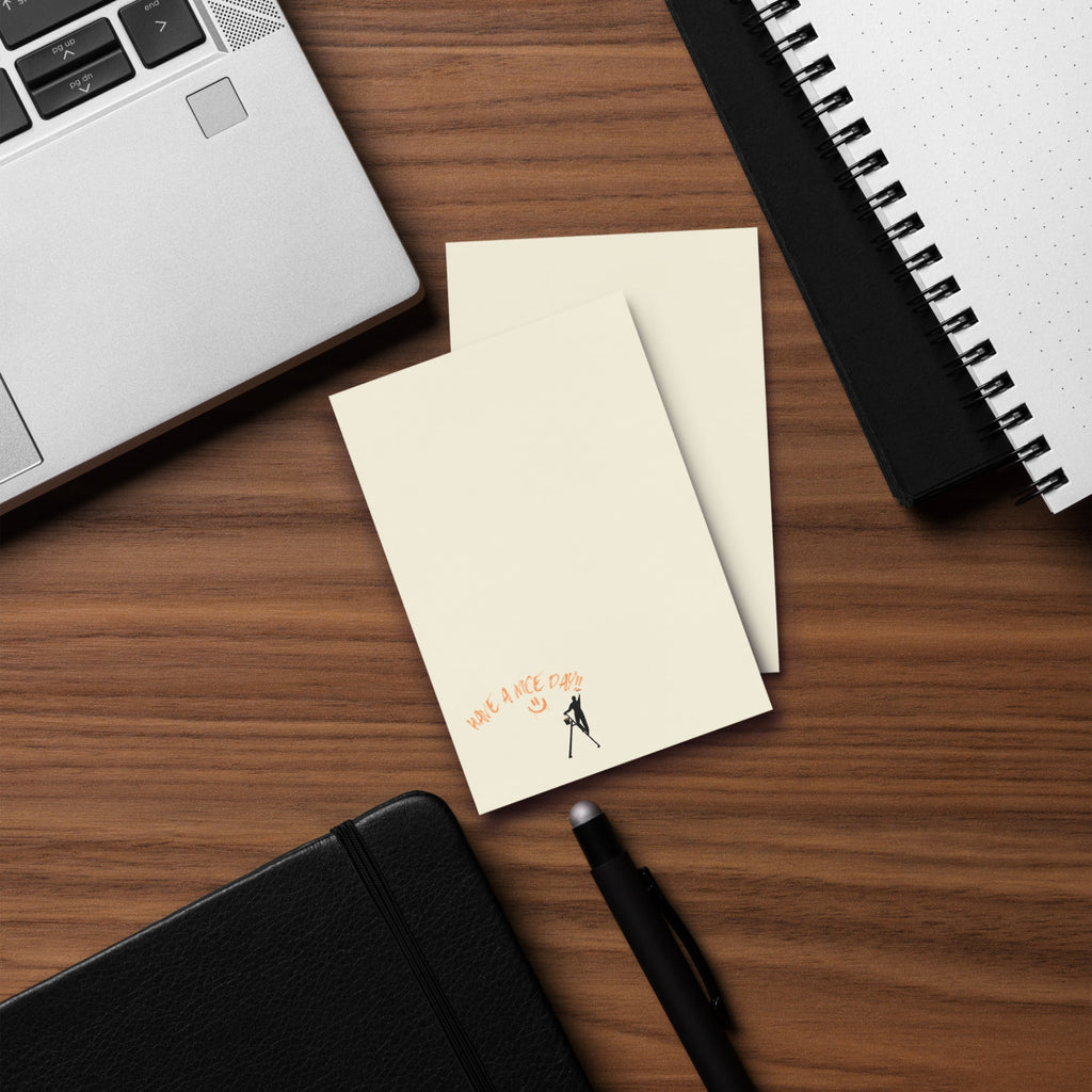 Beige large post it sticky note pad with black silhouette and text 'Have a nice day' on a wood desk with a laptop and  spiral notebook