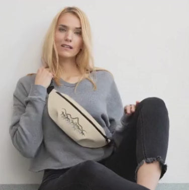 Blonde Woman put her phone in a beige fanny pack with a horse and mountains design of front. 