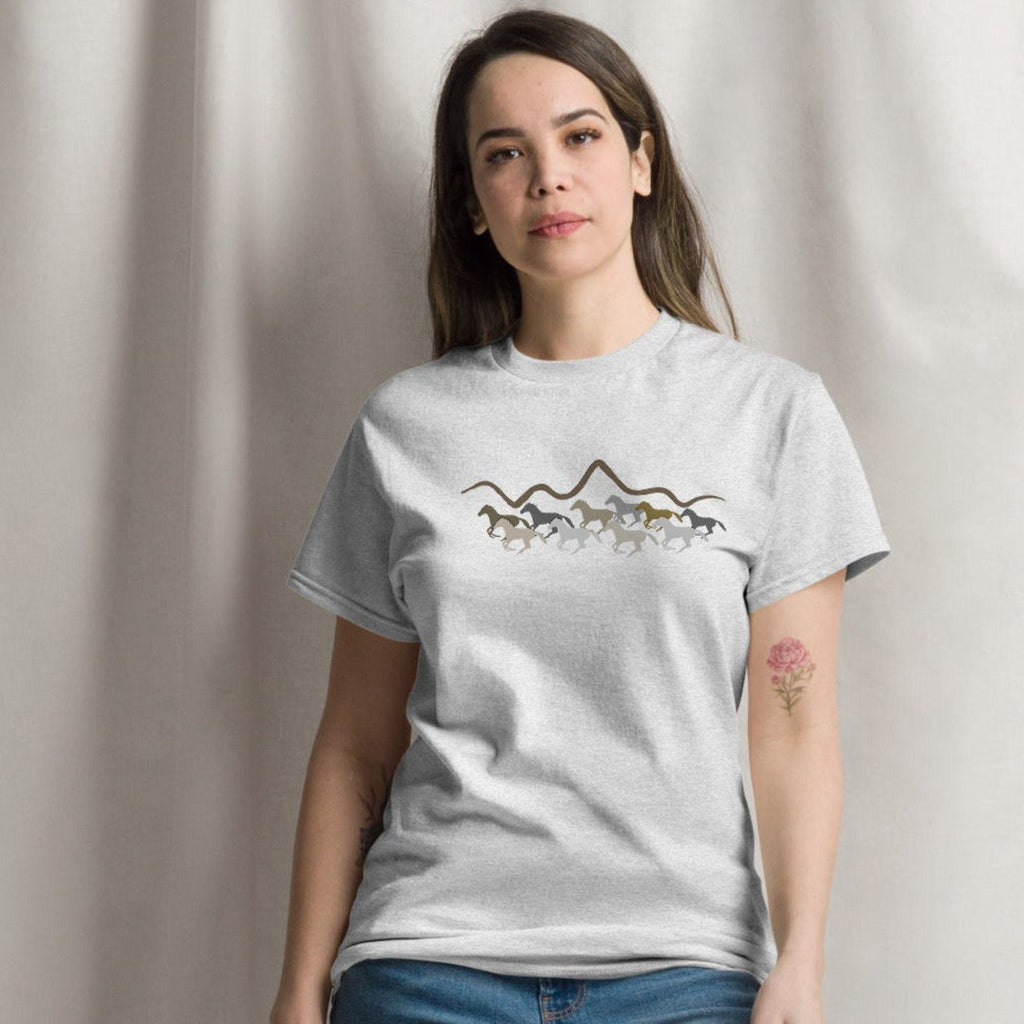 Woman wearing a grey graphic t-shirt featuring a wild mustang stampede and mountain design, styled casually for a western boho look. 