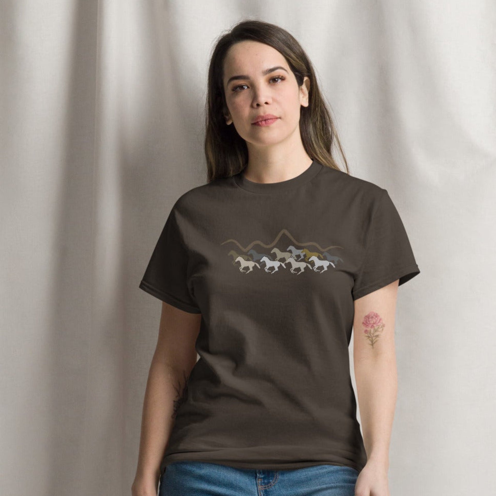 Woman wearing a brown graphic t-shirt featuring a wild mustang stampede and mountain design, styled casually for a western boho look