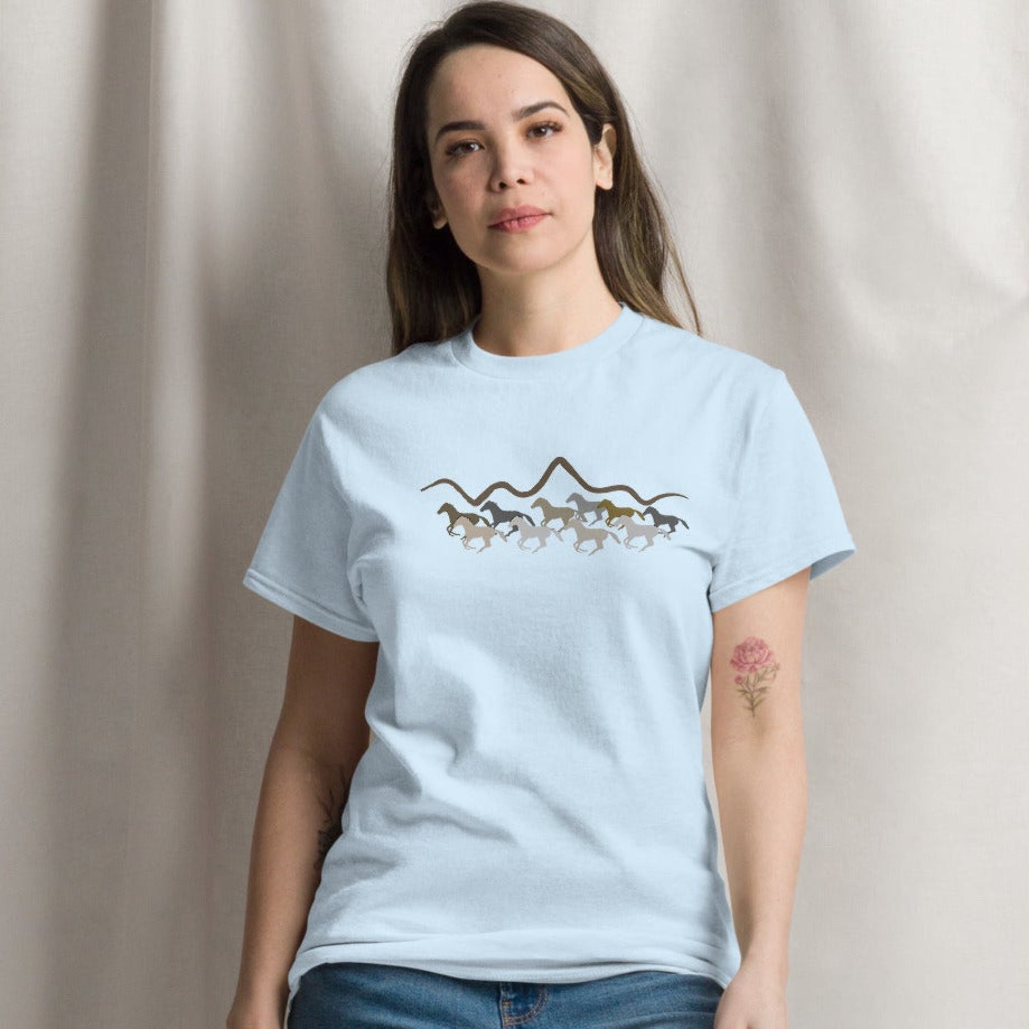 Woman wearing a light blue graphic t-shirt featuring a wild mustang stampede and mountain design, styled casually for a western boho look. 