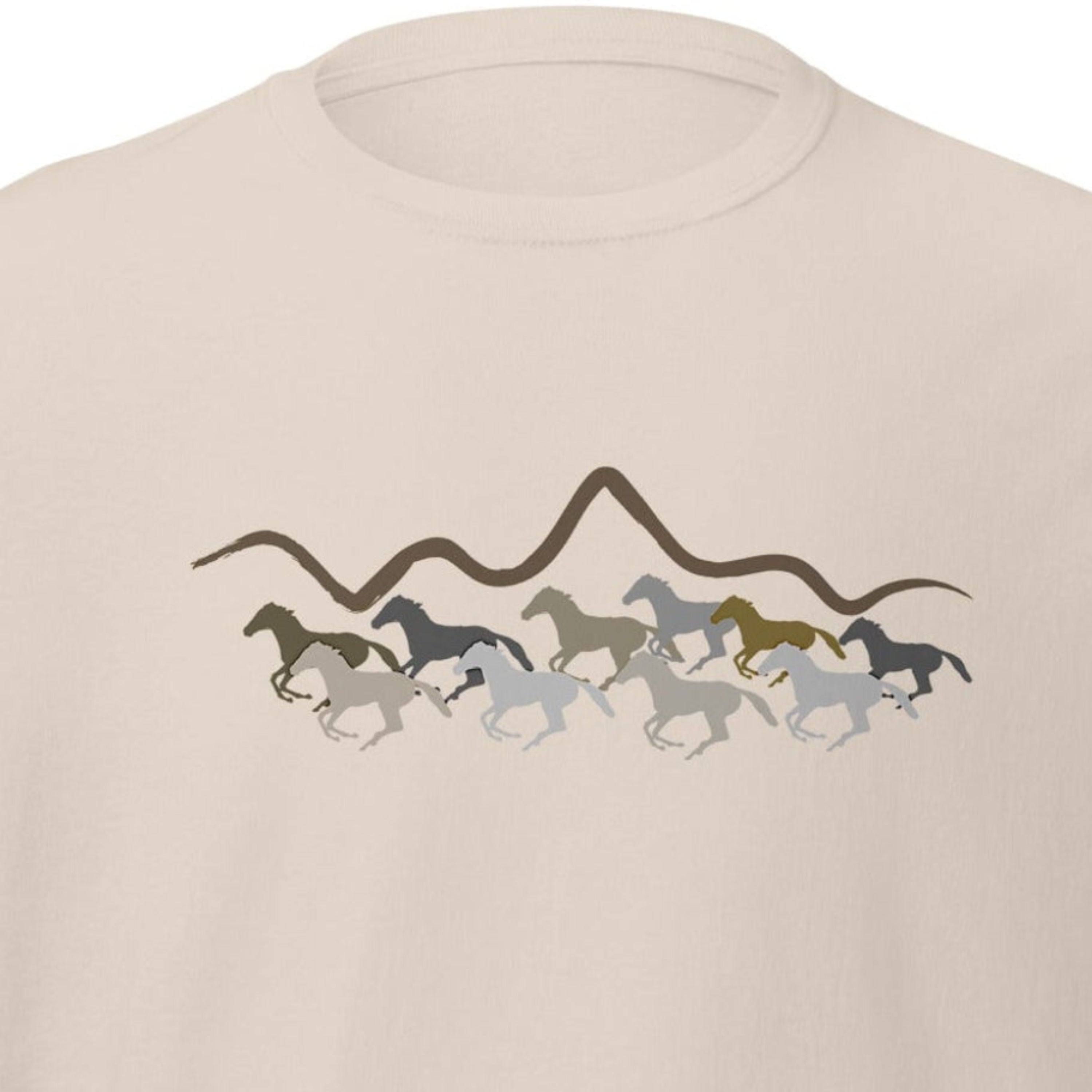 Sand beige unisex t-shirt with a running wild horses and mountain silhouette graphic design in earth tones, laid flat on a white background. 