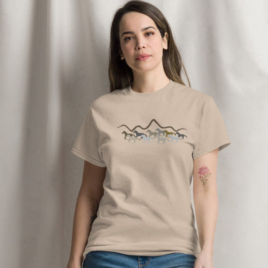 Woman wearing a sand beige graphic t-shirt featuring a wild mustang stampede and mountain design, styled casually for a western boho look. 