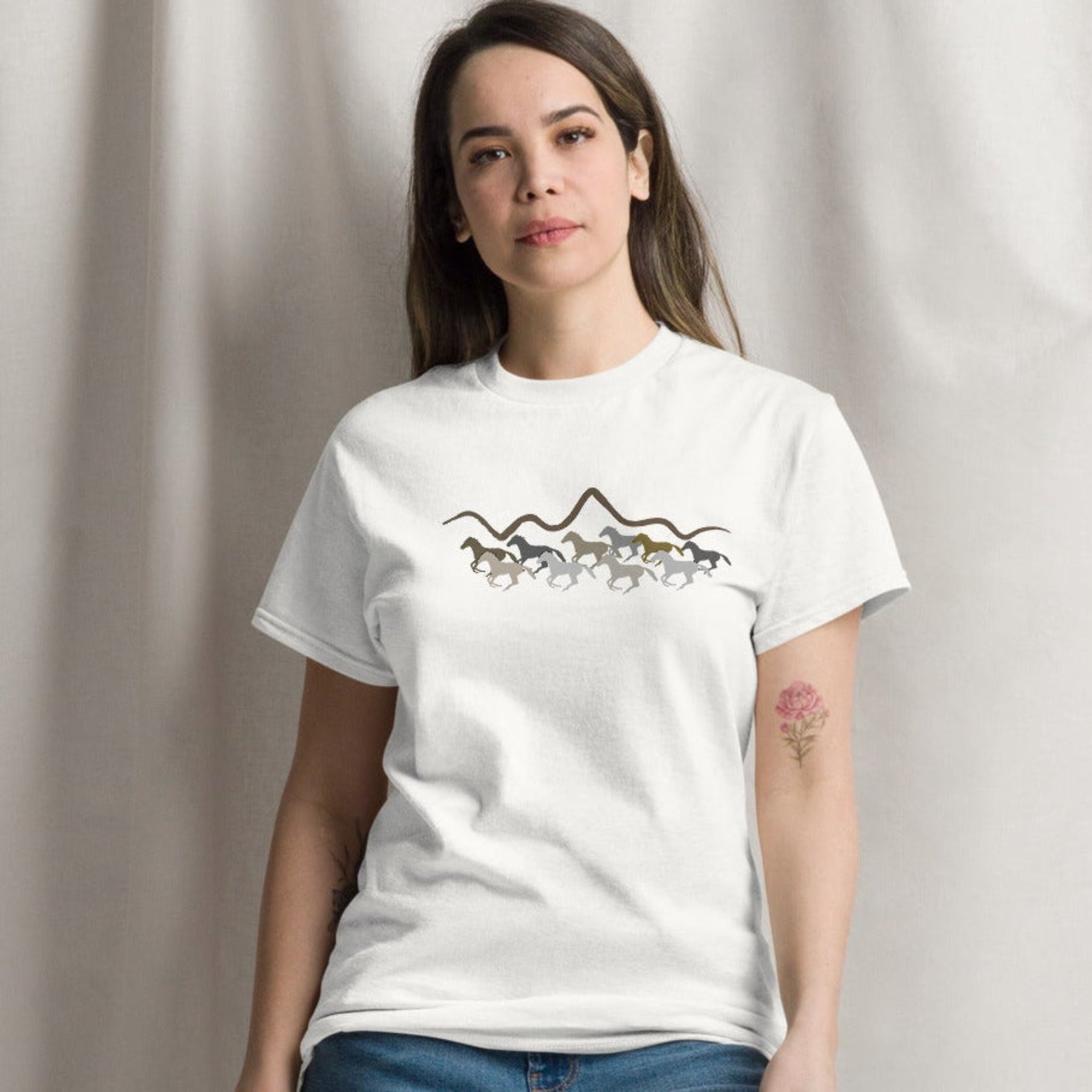 Woman wearing a white graphic t-shirt featuring a wild mustang stampede and mountain design, styled casually for a western boho look. 