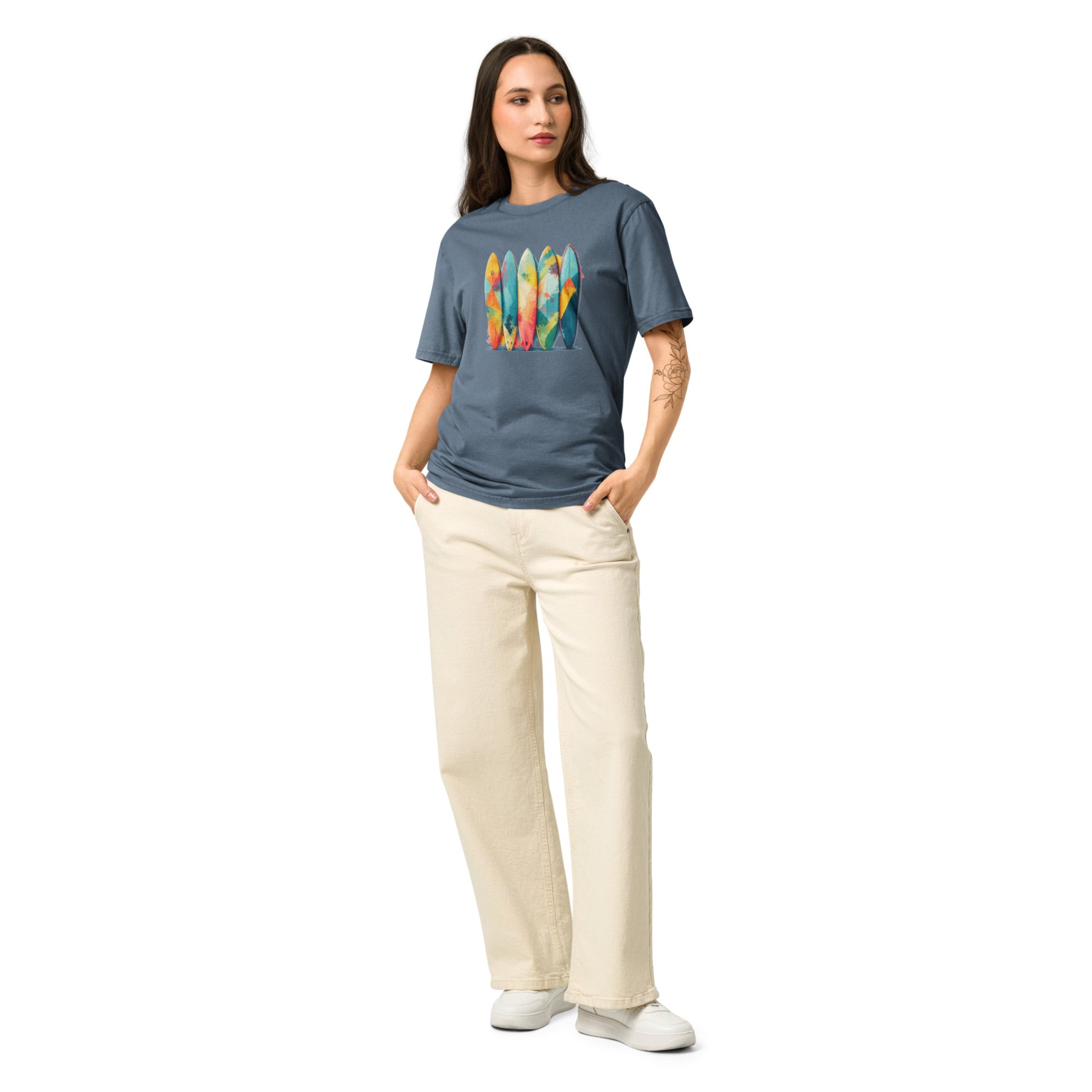 Woman wearing a blue t-shirt with a colorful surfboard design and beige pants on a white background.