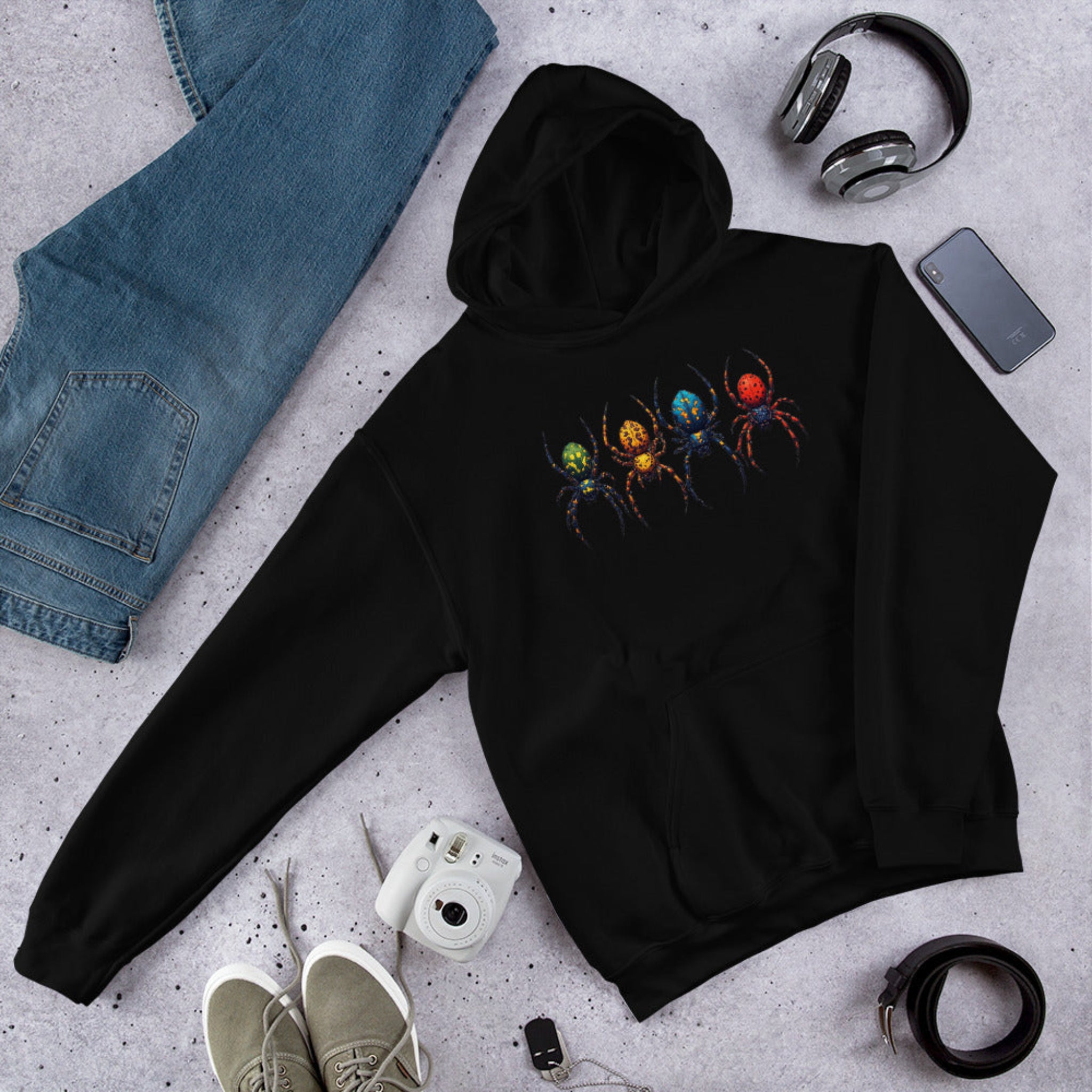 Black hoodie with a colorful spider design on a gray surface with jeans, shoes, and accessories.