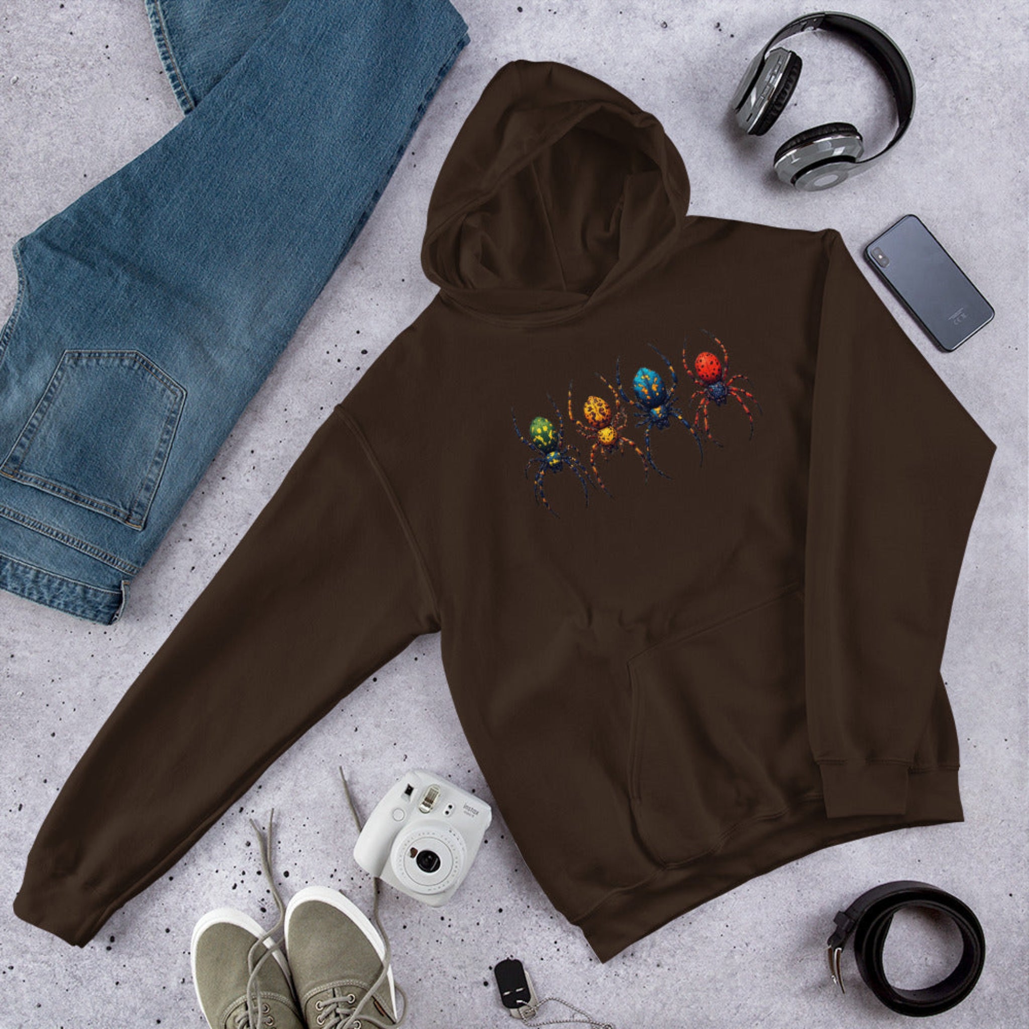 Brown hoodie with a colorful spider design on a gray surface with jeans, shoes, and accessories.