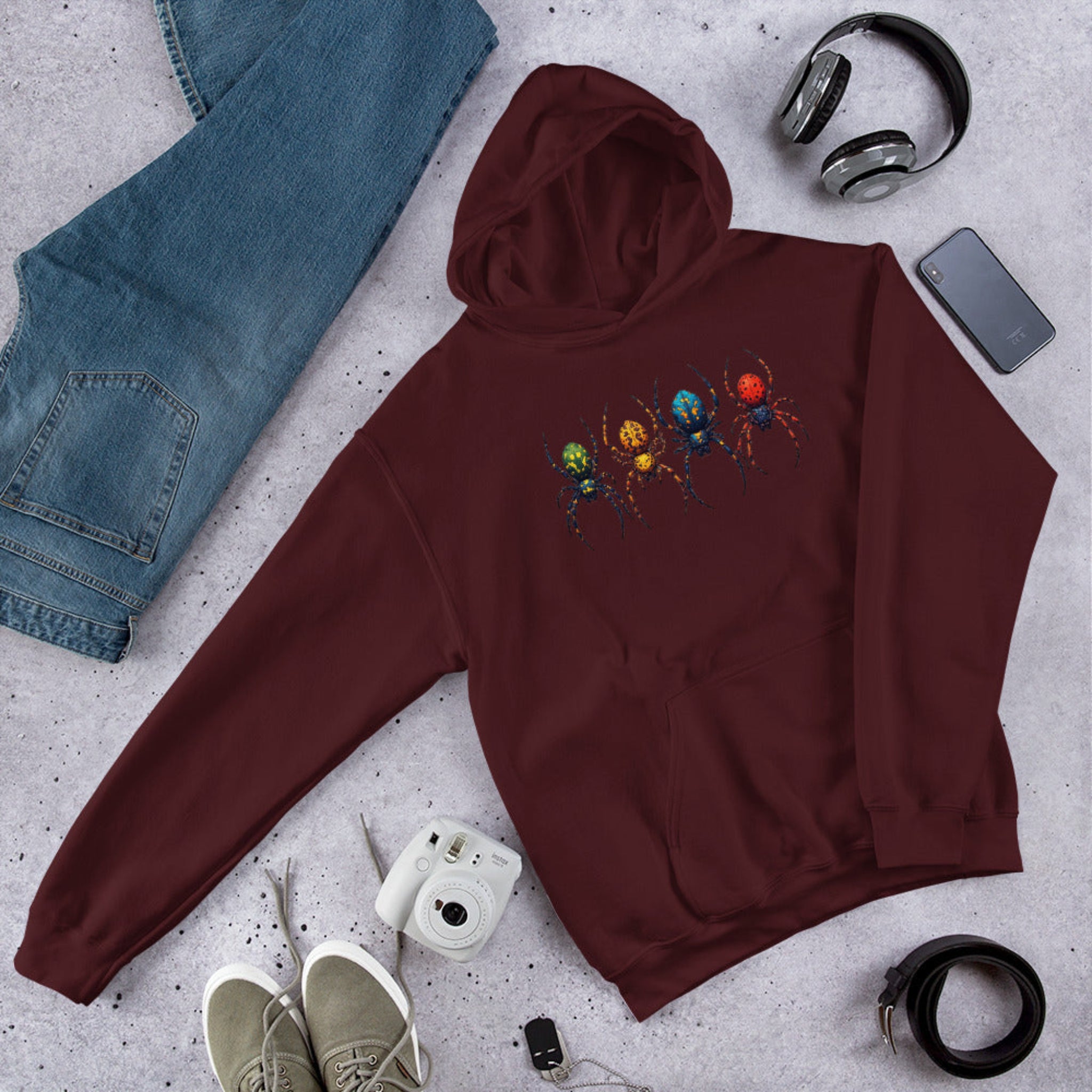 Maroon hoodie with a colorful spider design on a gray surface with jeans, shoes, and accessories.