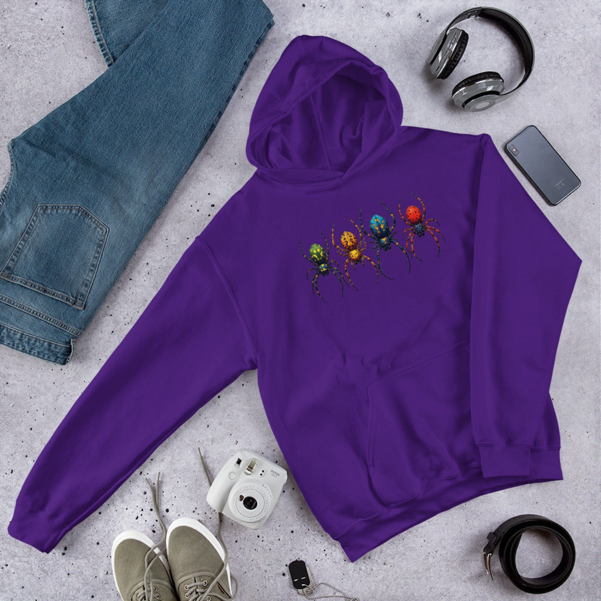 Purple hoodie with a colorful spider design on a gray surface with jeans, shoes, and accessories.