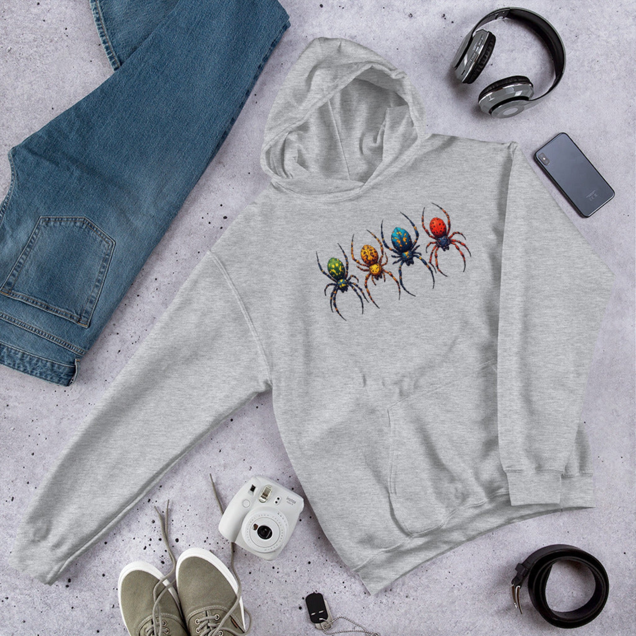 Gray hoodie with a colorful spider design on a gray surface with jeans, shoes, and accessories.