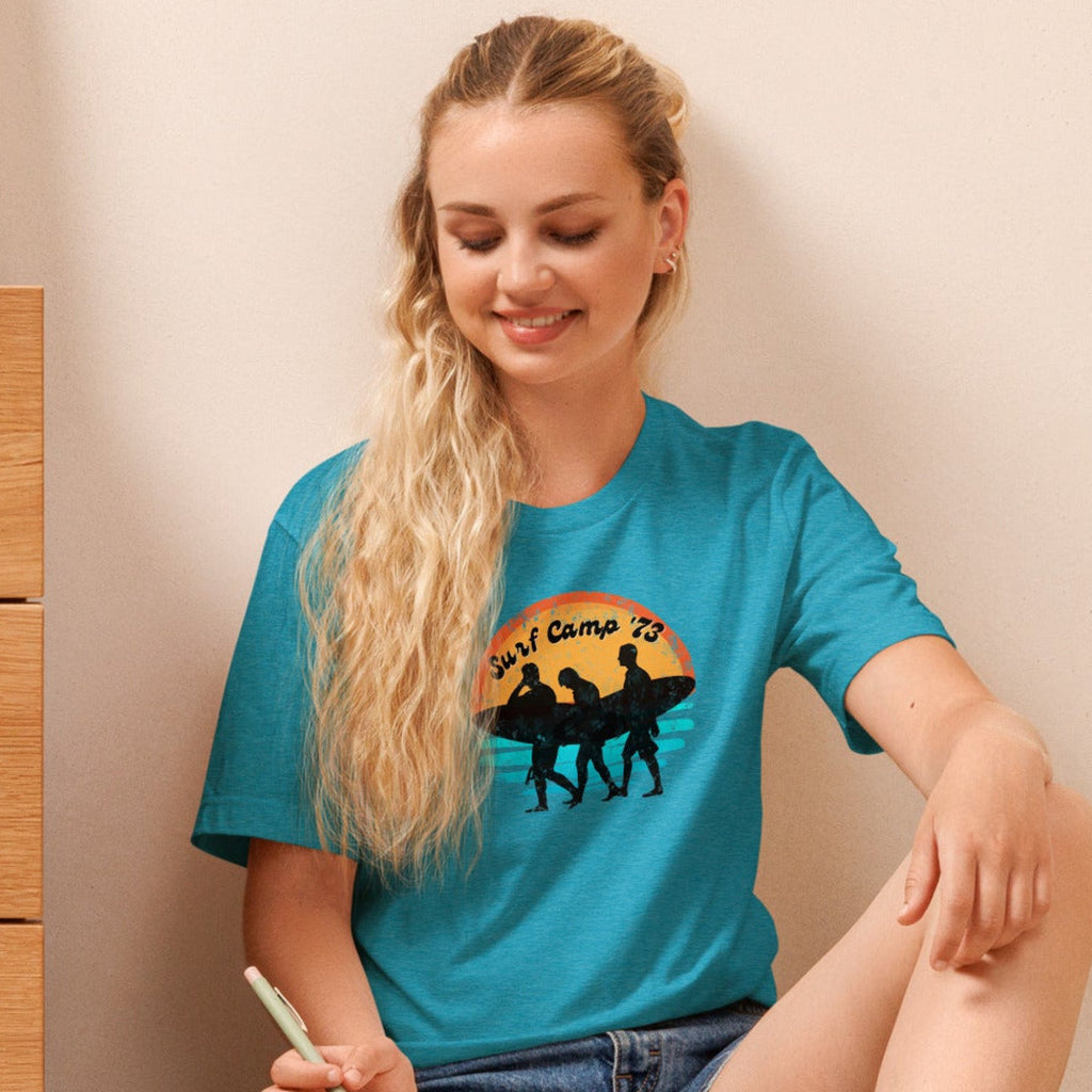 Woman sitting on the floor reading a book wearing a t-shirt with 'Surf Camp 73' distressed vintage design on front of t-shirt.