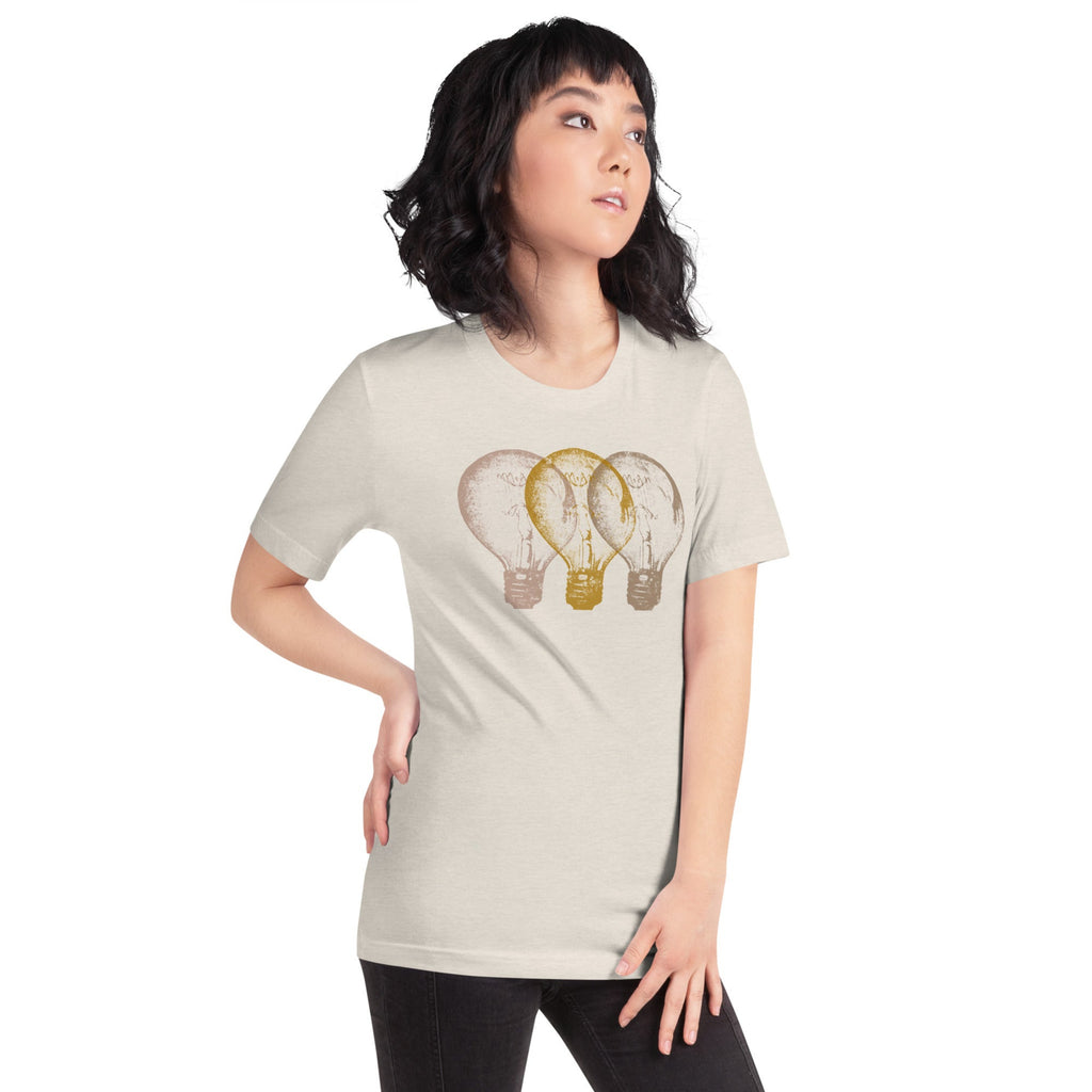 Woman wearing a light beige t-shirt with an Edison light bulb graphic design, standing against a white wall.