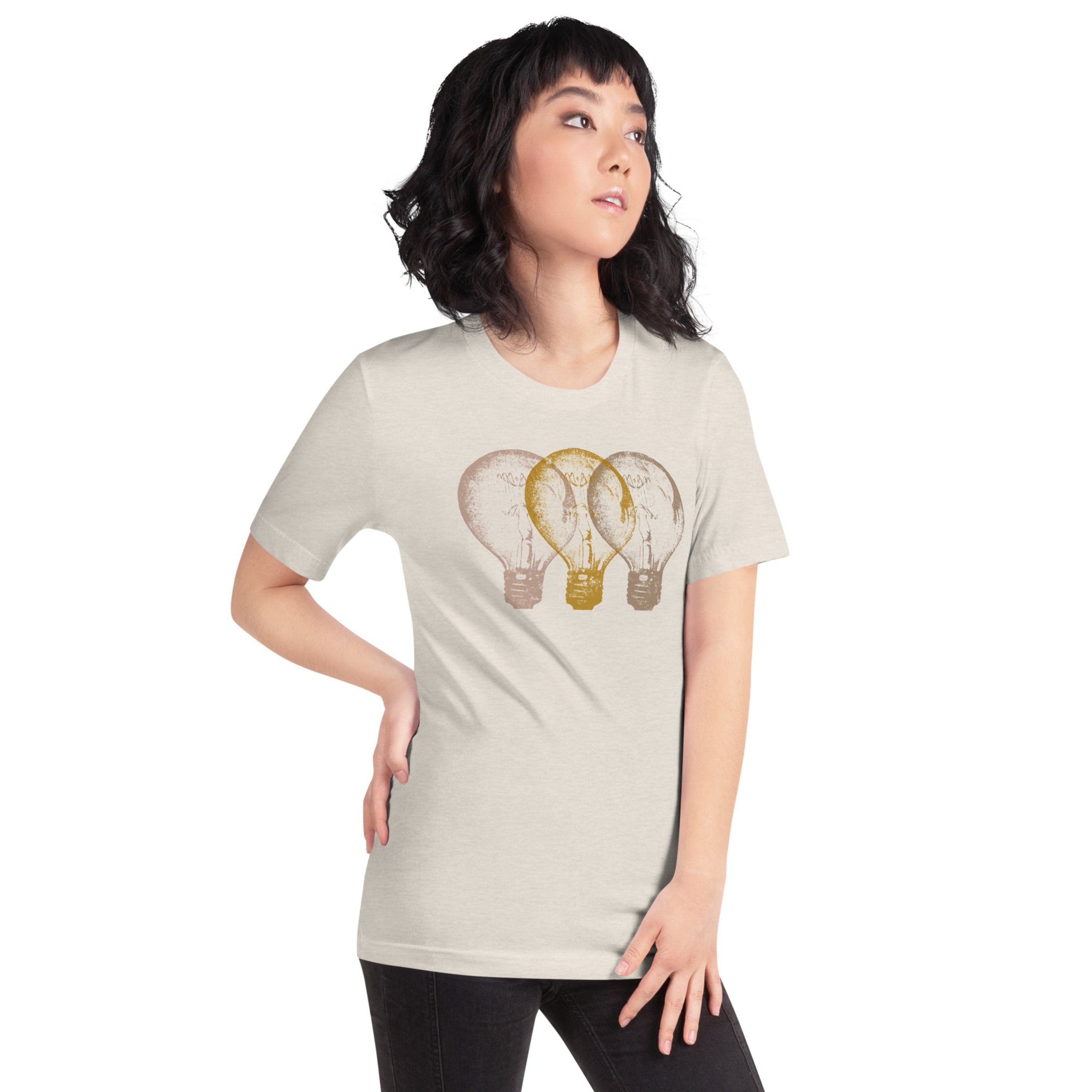 Woman wearing a light beige t-shirt with an Edison light bulb graphic design, standing against a white wall.