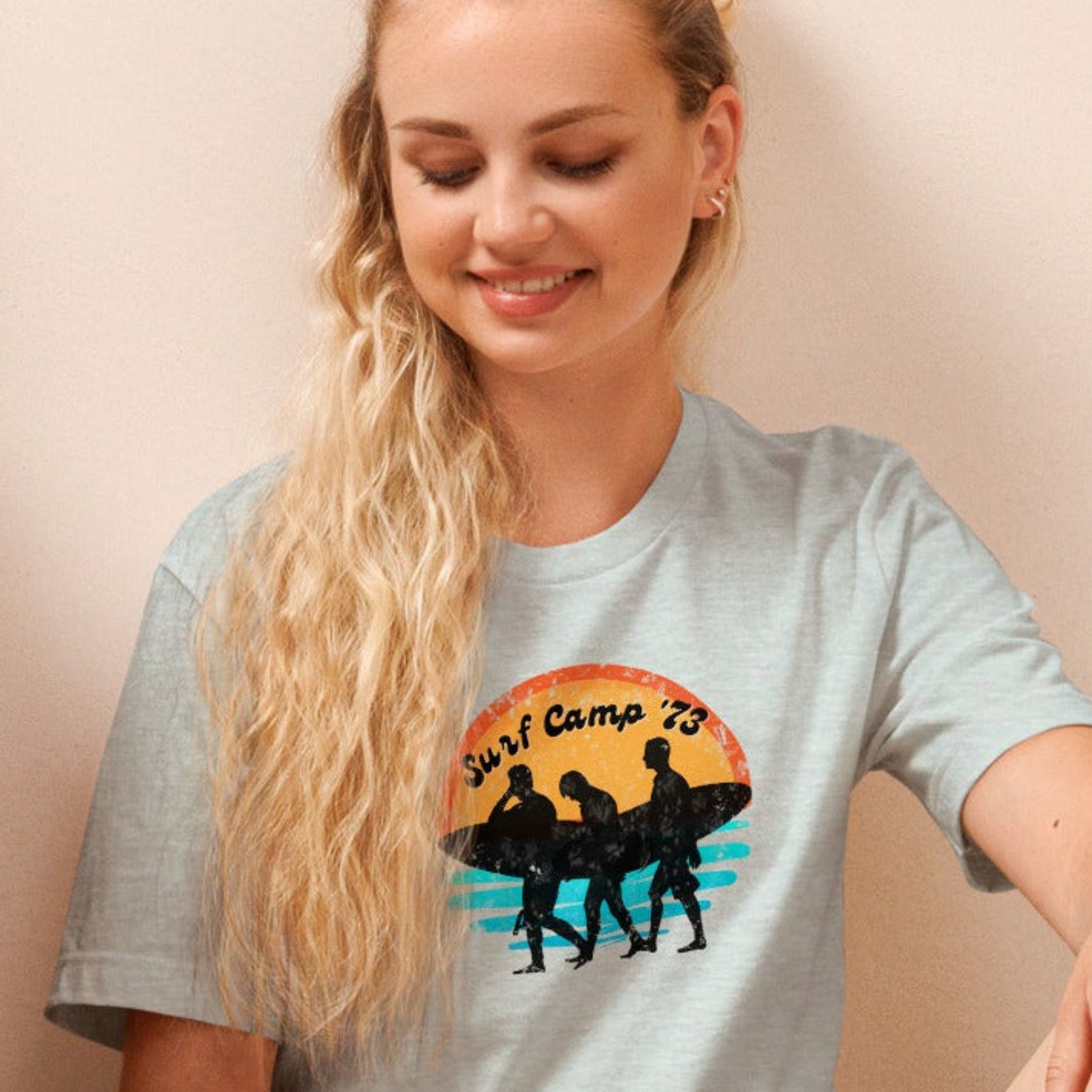 Woman sitting on the floor reading a book wearing a t-shirt with 'Surf Camp 73' distressed vintage design on front of t-shirt.