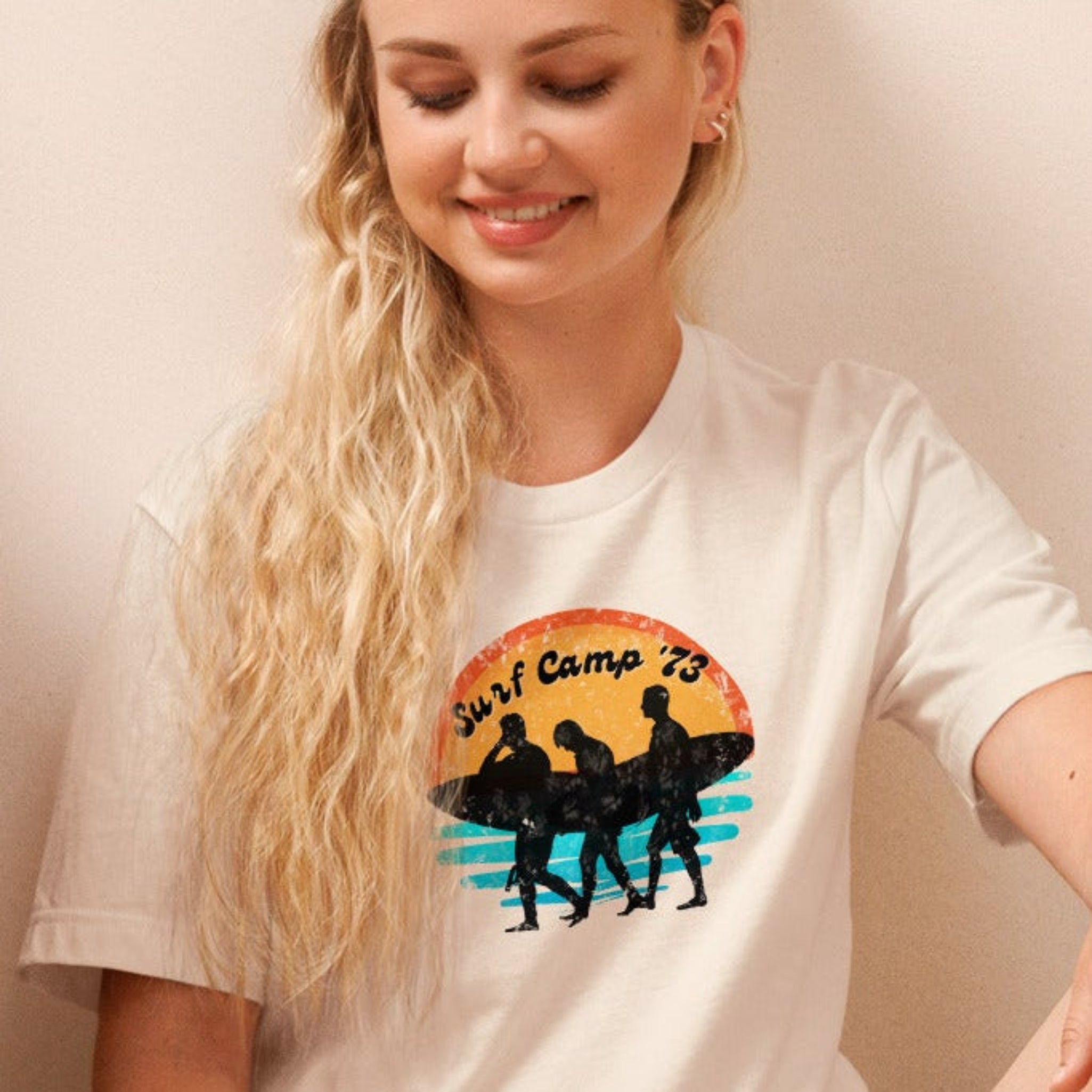 Woman sitting on the floor reading a book wearing a t-shirt with 'Surf Camp 73' distressed vintage design on front of t-shirt.