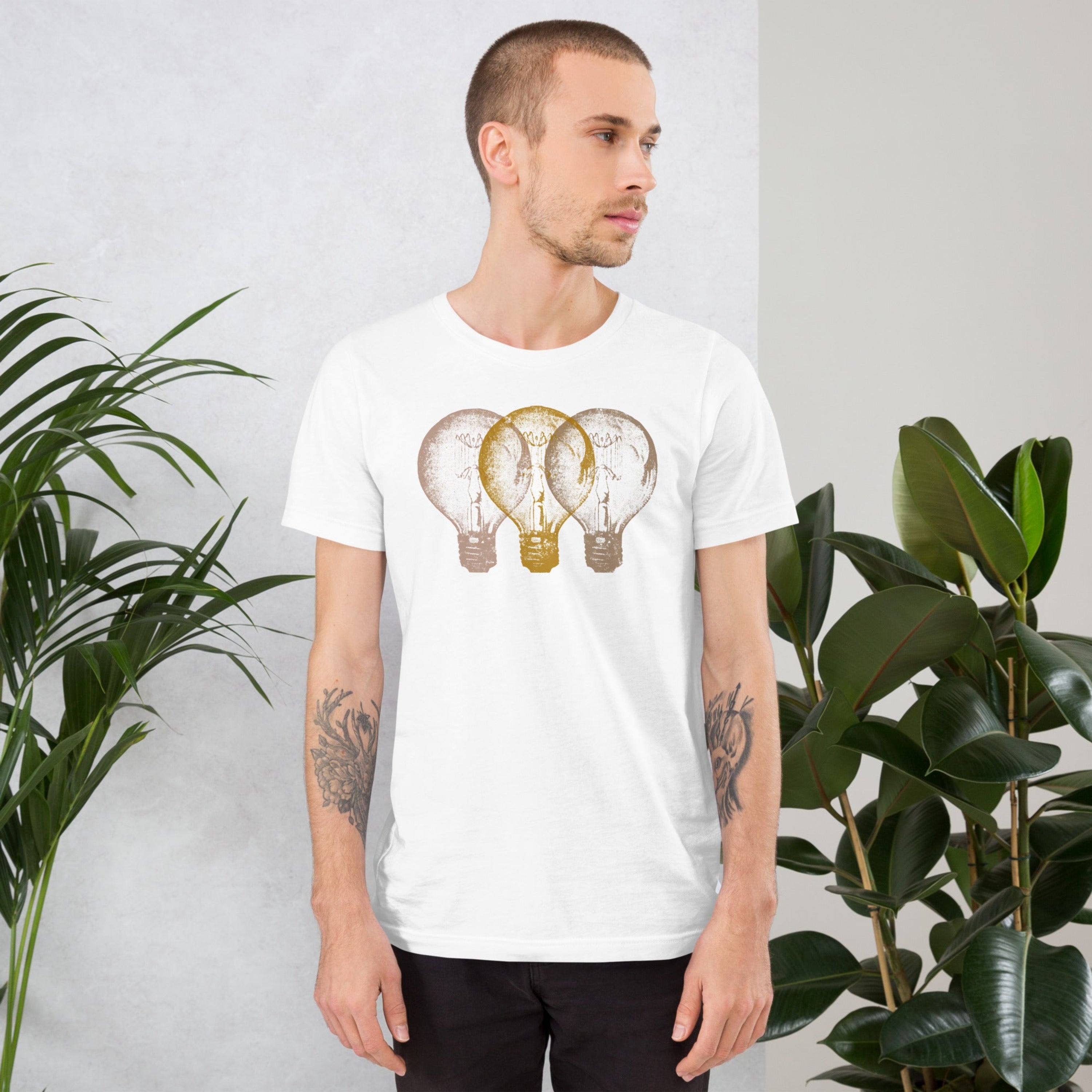 Man wearing a white t-shirt with an Edison light bulb design standing against a light gray background with plants.
