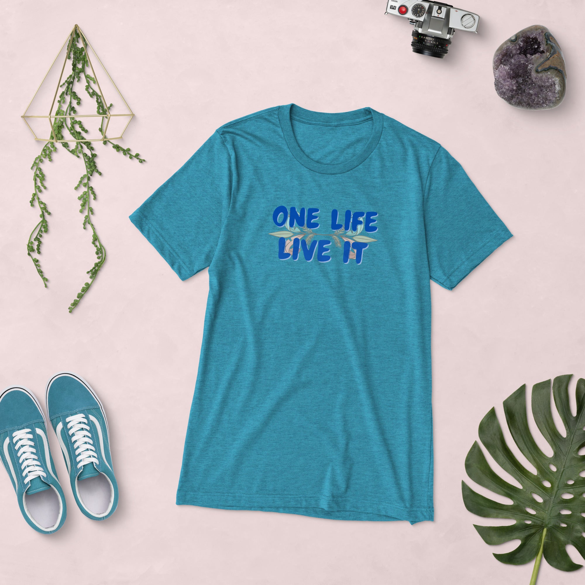 Blue t-shirt with 'One Life, Live It' text on a light pink background with shoes and decor items.
