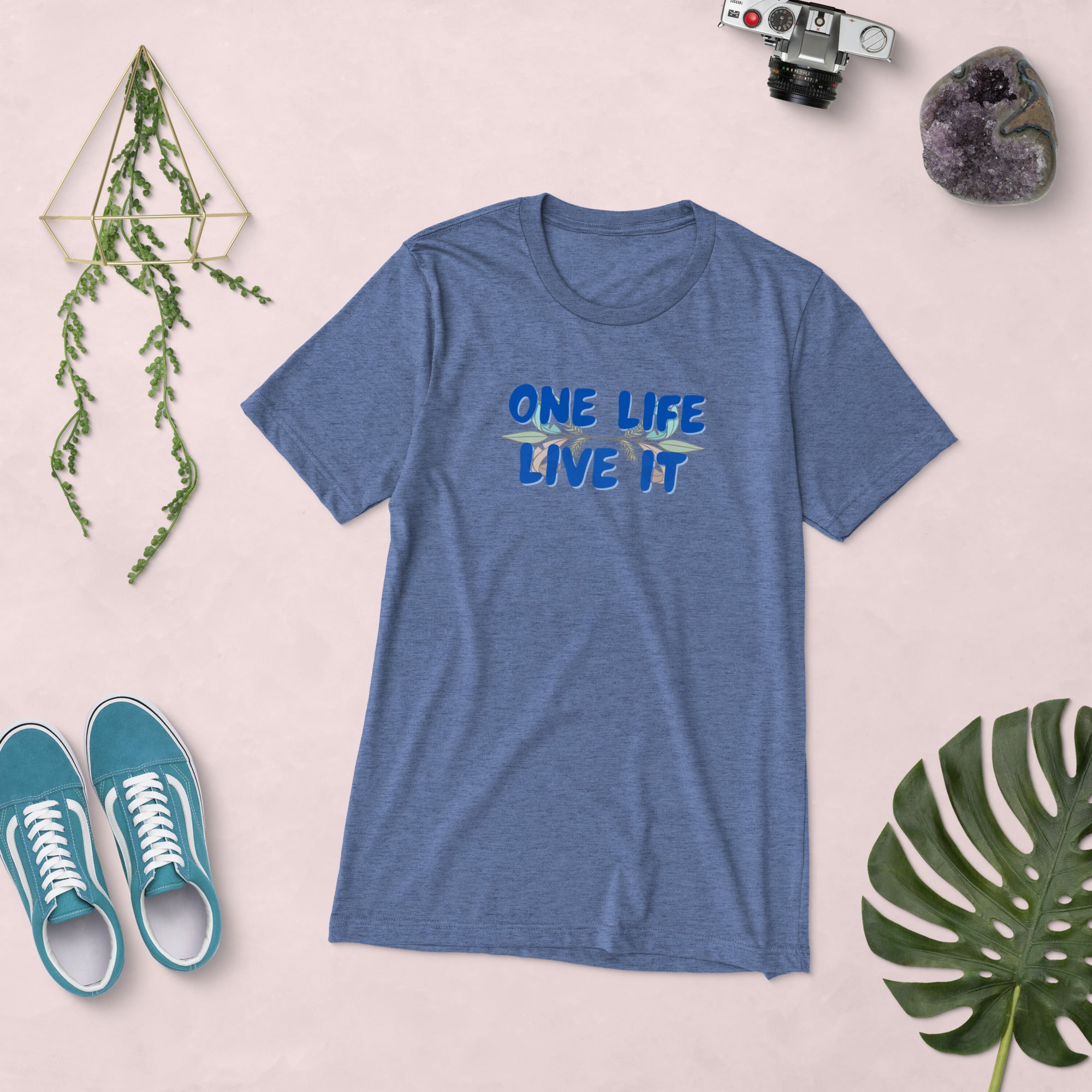 Blue t-shirt with 'ONE LIFE LIVE IT' text, teal sneakers, and decorative items on a light pink background.