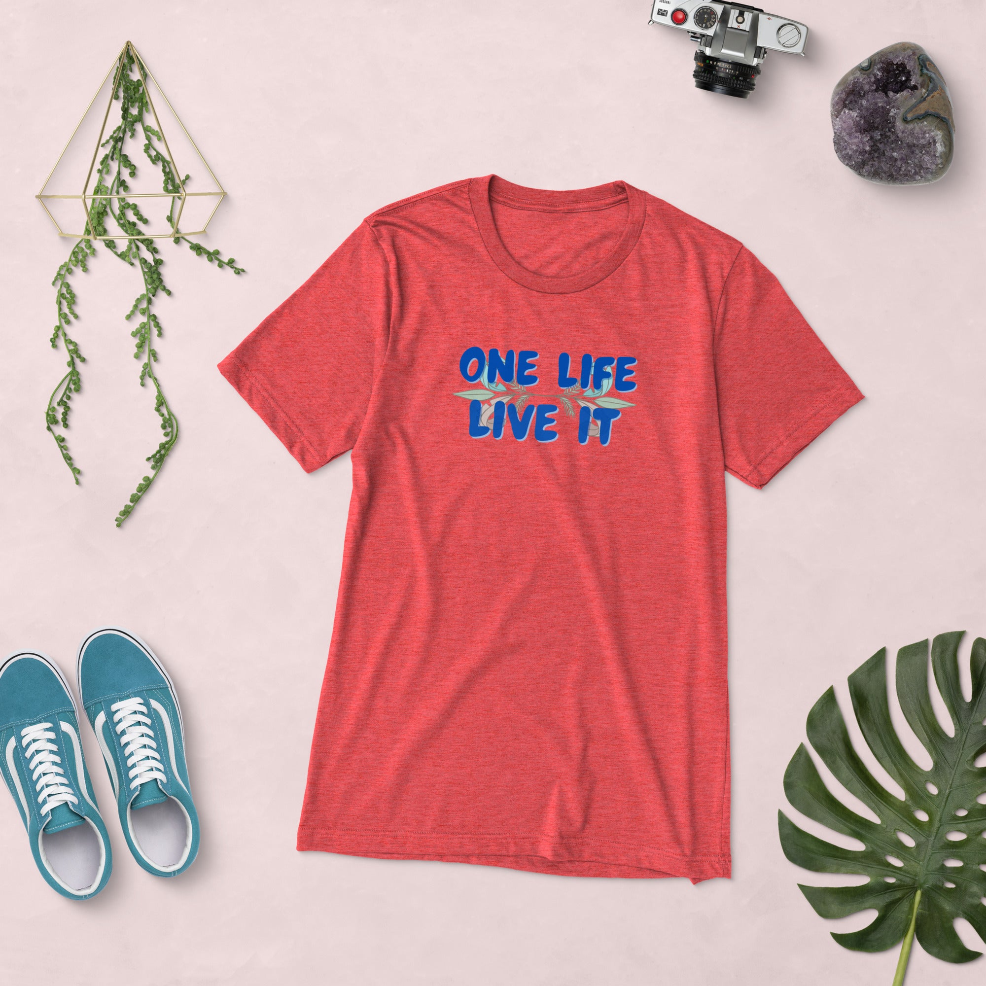 Red t-shirt with 'ONE LIFE LIVE IT' text, blue sneakers, and decorative items on a light pink background.