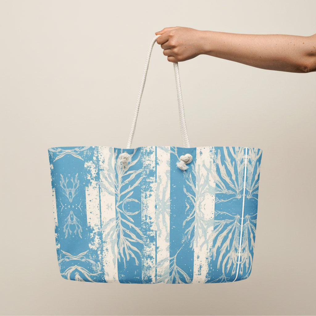 Tote bag with blue and white leaf pattern held by a hand on a white background.
