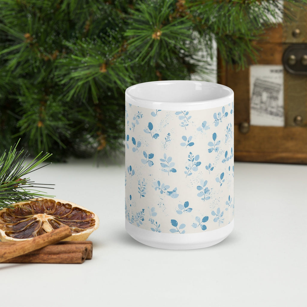 White mug with blue floral pattern on a white surface with Christmas decorations.