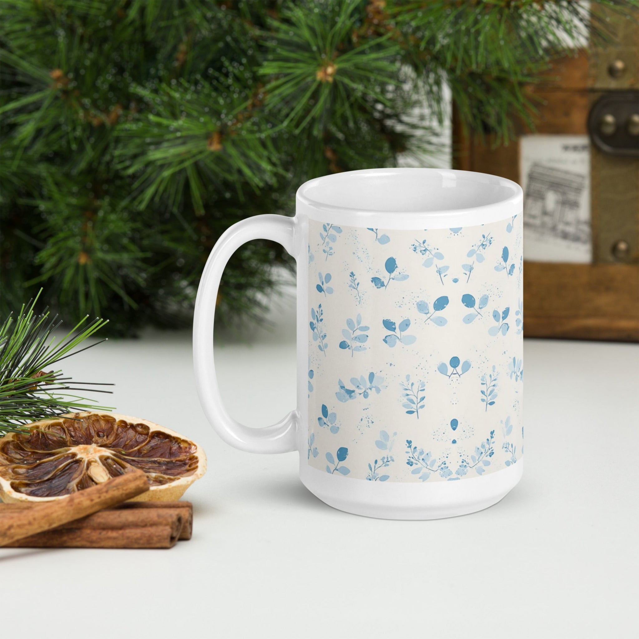 White mug with blue floral pattern on a white surface with Christmas decorations.