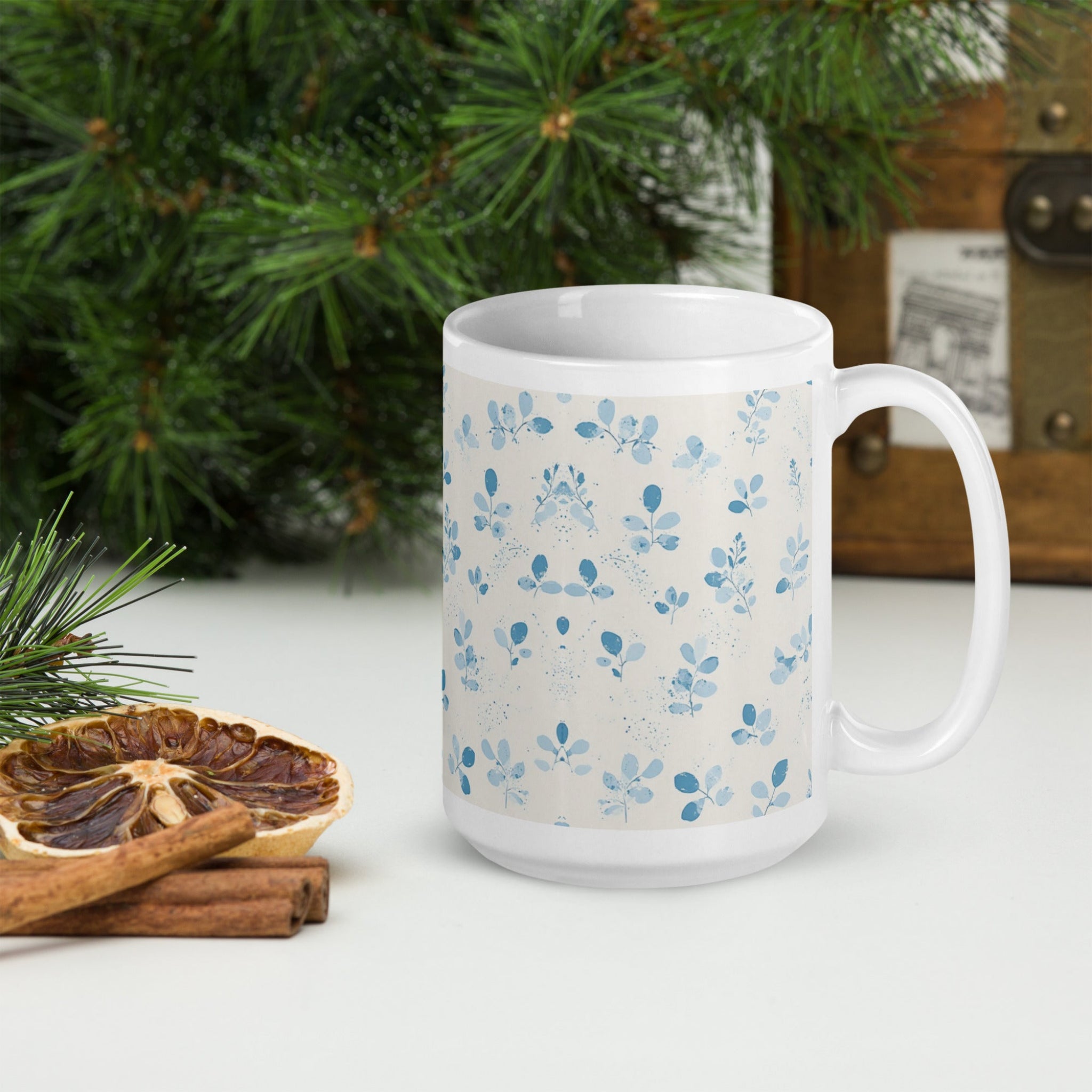 White mug with blue floral pattern on a white surface with Christmas decorations.