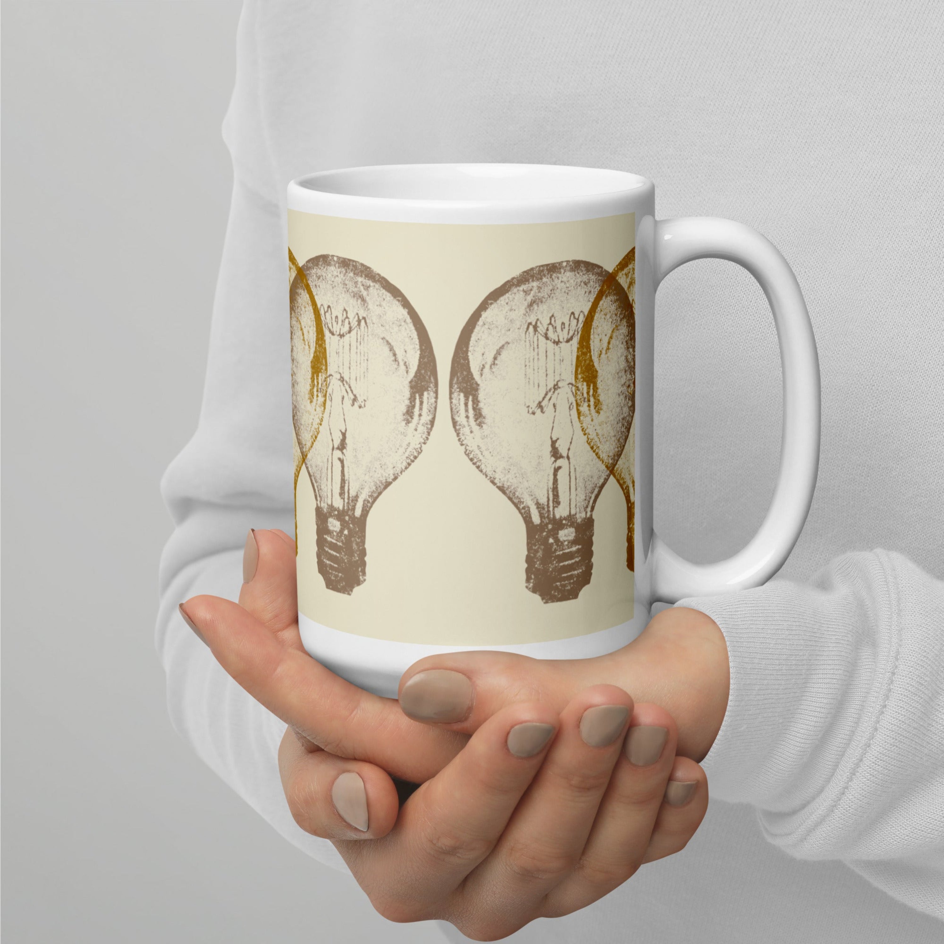 Person holding a mug with light bulb design on a plain background.