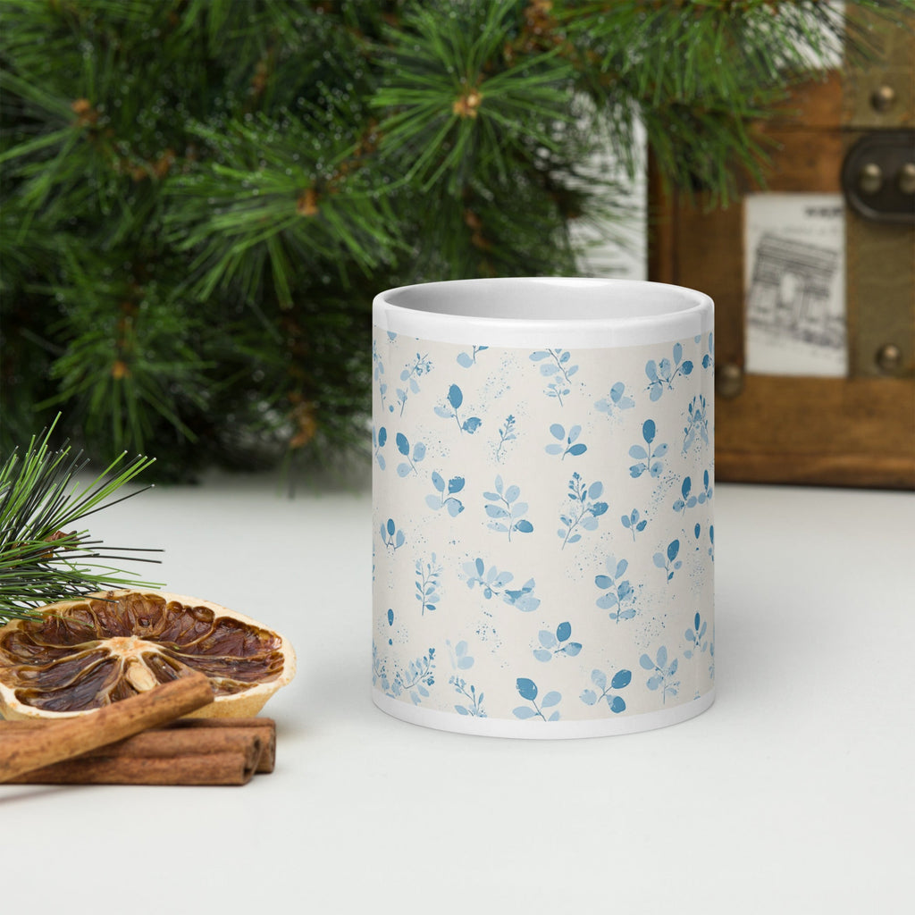 White mug with blue floral pattern on a white surface with Christmas decorations.