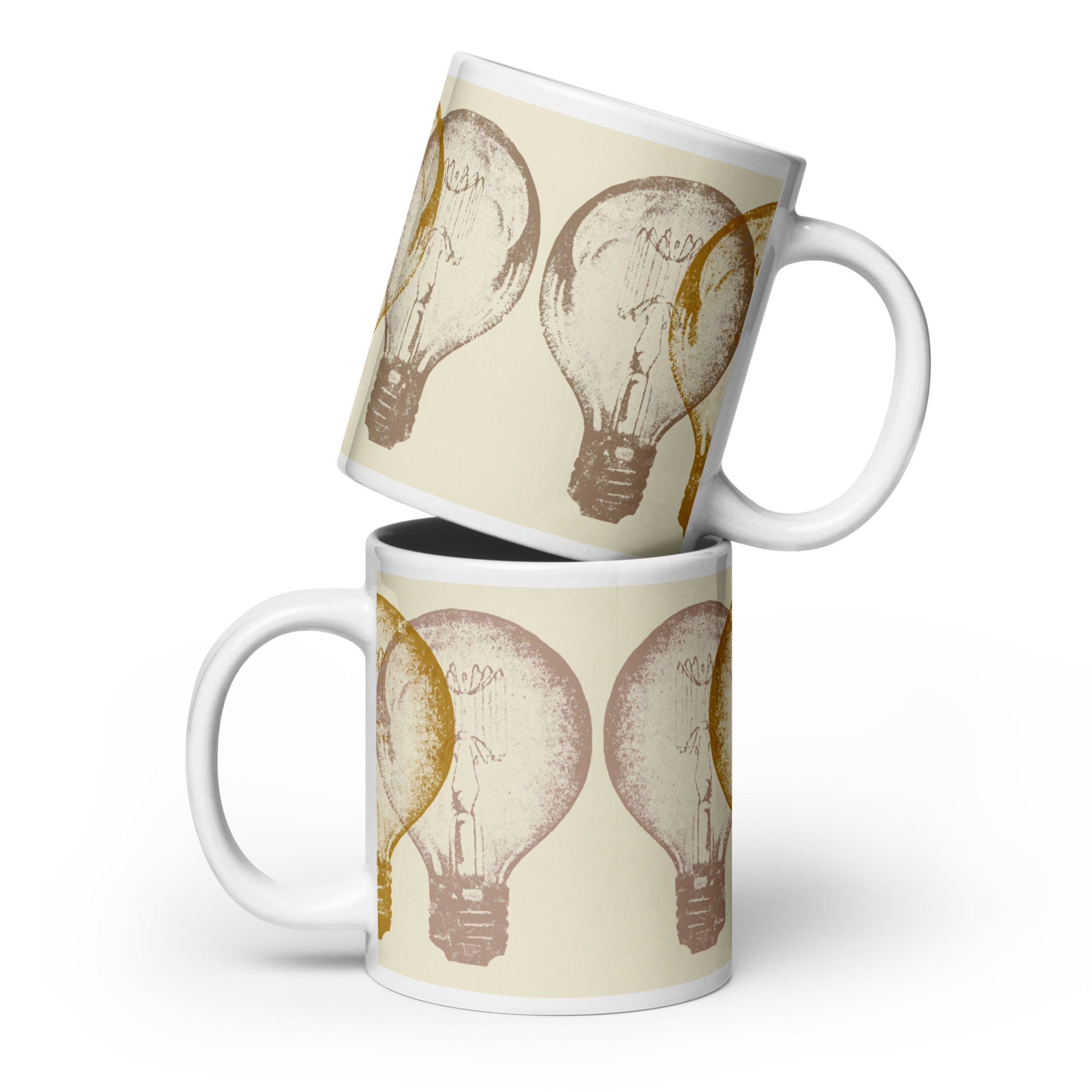White ceramic coffee mug with vintage engraving-style lightbulb illustration in gold and mauve tones on a cream background, shown in two stacked sizes.