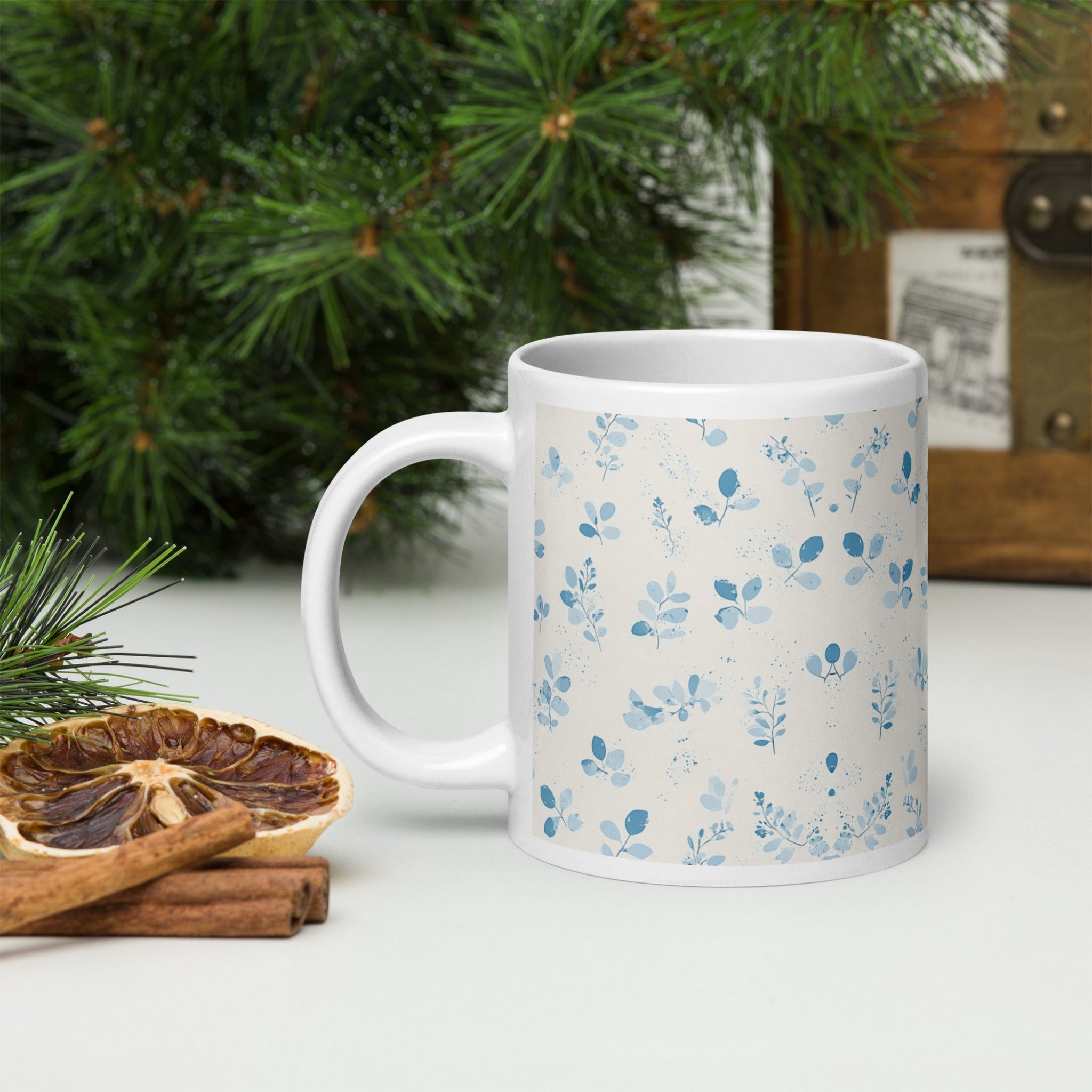 White mug with blue floral pattern on a white surface with Christmas decorations.