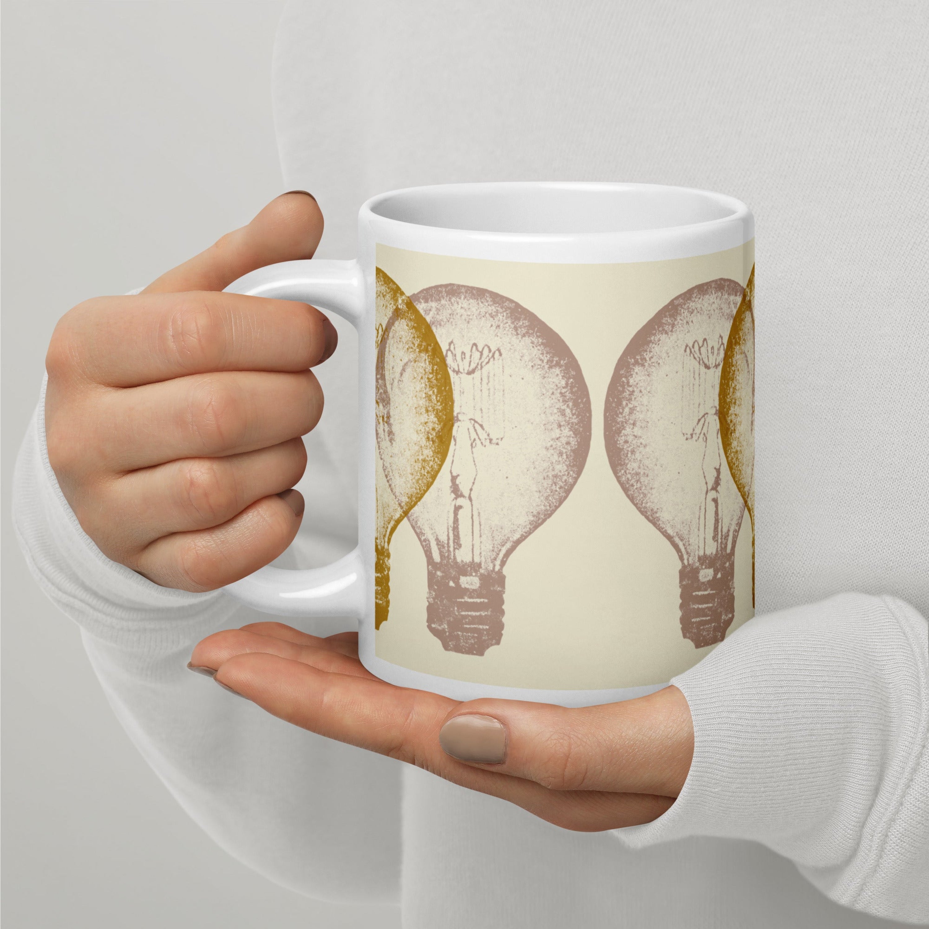 Hand holding a mug with light bulb design on a plain background.