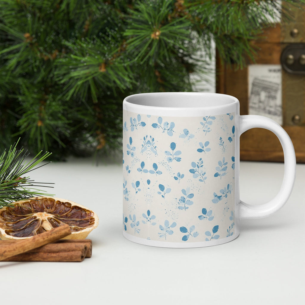 White mug on a surface with Christmas decorations including pine branches and cinnamon sticks.